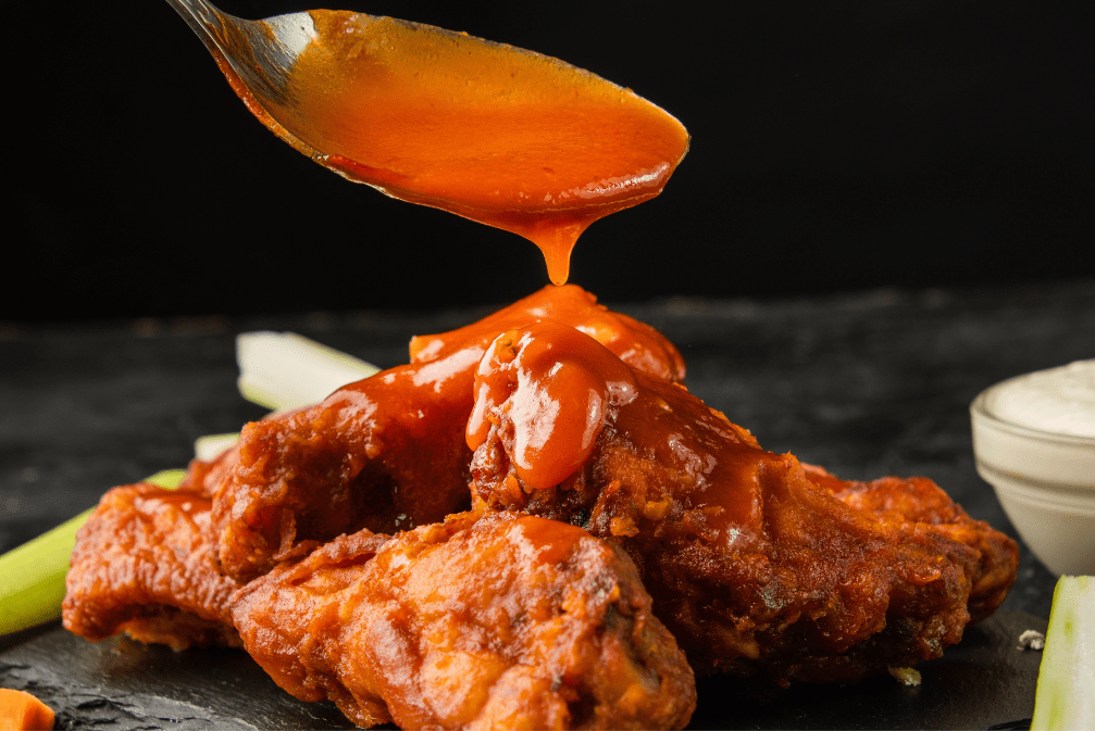 sweet and spicy sauce and red sauce in ramekins with raw ingredients on a black surface